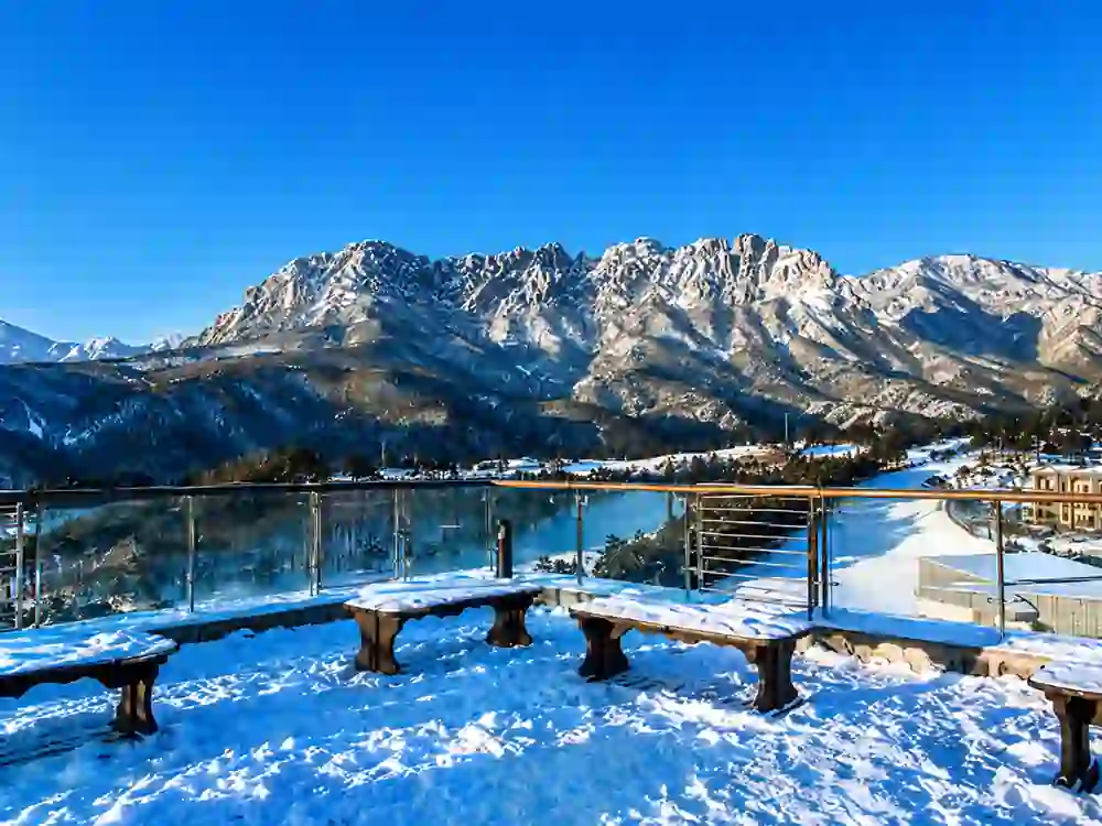 Snow-covered mountain landscape with a scenic viewing deck overlooking a frozen valley and majestic peaks under a clear blue sky in Kashmir.